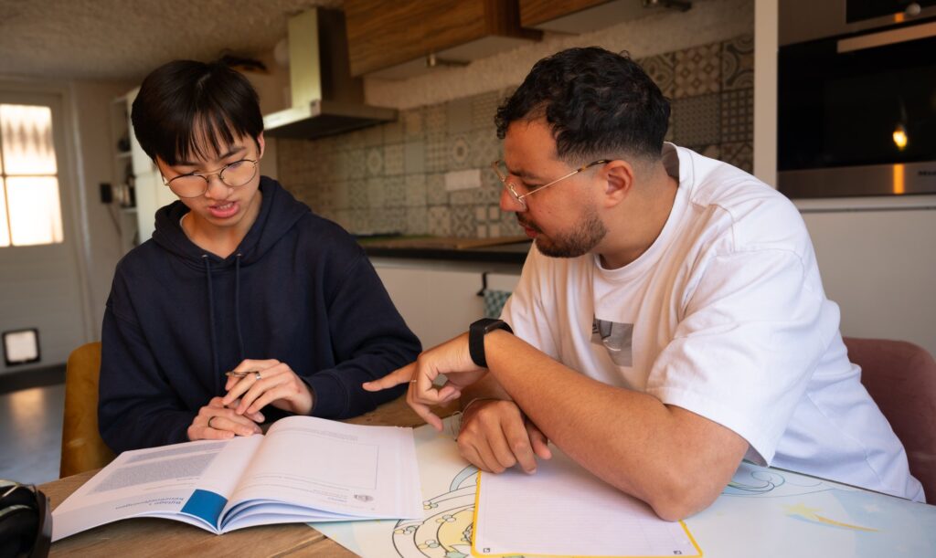 Begeleider en jongere werken samen in een werkboek aan tafel